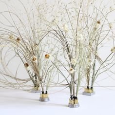 three metal vases with flowers in them on a white tableclothed surface, one is filled with dried grass and the other has gold colored stems