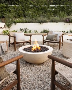 an outdoor fire pit surrounded by chairs and tables with plants on the side wall behind it