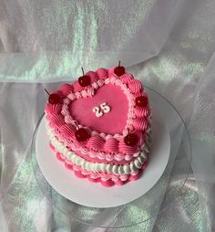 a pink heart shaped cake on a plate with the number 25 written on it and two cherries in the middle