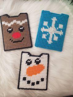 three cross stitch coasters with animals and snowflakes on them sitting on a white furnishing