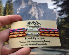 a person holding two colorful bracelets with mountains in the backgroung background