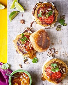 three burgers with toppings on a table next to a bowl of salsa and lime