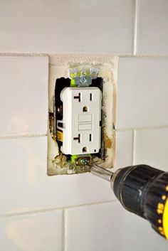 a person using a drill to fix an electrical outlet in a wall with white tiles