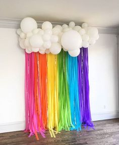 balloons and streamers are hanging from the ceiling in front of a rainbow colored wall