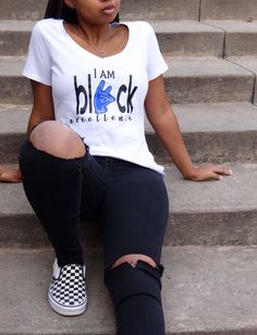 a woman sitting on the steps with her legs crossed and wearing black ripped jeans, a white t - shirt that says i am black excellence