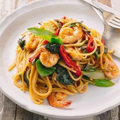 a white plate topped with pasta covered in shrimp and veggies next to a fork