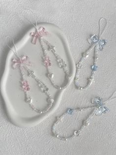 three pieces of jewelry are sitting on a white platter with beads and bows hanging from it