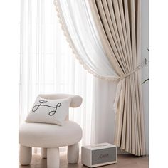 a white chair sitting in front of a window with curtains and a pillow on top of it