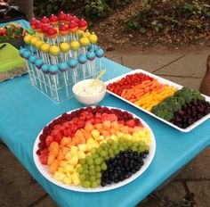 a table topped with plates of fruit and veggies next to cupcakes