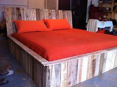 a bed made out of pallet wood with orange sheets and pillows on the headboard