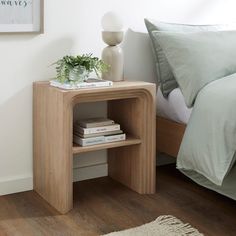 a nightstand with books on it next to a bed