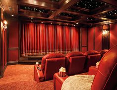 an empty theater with red curtains and leather recliners in front of the screen