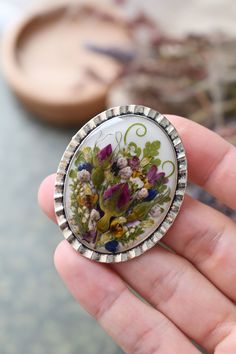 a person holding a brooch with flowers on it's side in their hand