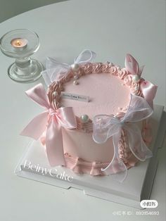 a pink cake decorated with bows and pearls on top of a white box next to a candle