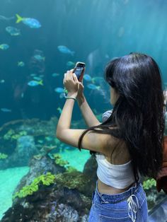 a woman is taking a photo in front of an aquarium with her cell phone while looking at the fish