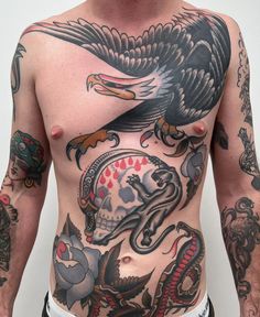 a man with an eagle tattoo on his chest is standing in front of a white wall