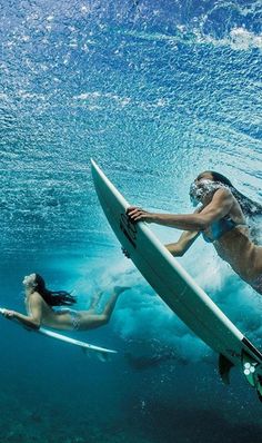 two people are swimming in the ocean with their surfboards and one is holding a surfboard