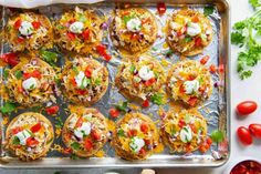 an overhead shot of mexican style mini tacos on a baking sheet with tomatoes, cilantro and sour cream