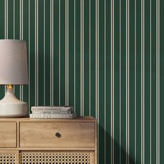 a lamp sitting on top of a wooden dresser next to a green striped wallpaper