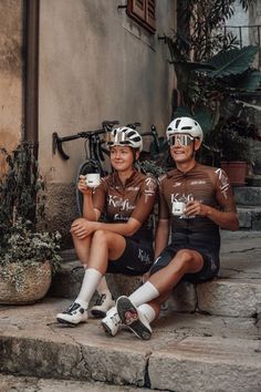 two people sitting on the steps with their bikes and drinking from cups in front of them