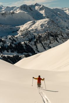 a person riding skis on top of a snow covered slope with mountains in the background