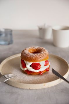 a donut with strawberries and cream on it sitting on a plate next to a fork