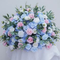 a bouquet of blue and pink flowers sitting on top of a white cloth covered table