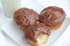 three chocolate frosted cupcakes on a plate next to a glass of milk