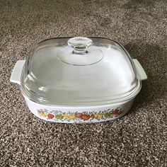 a glass casserole dish with a lid on carpeted floor next to wall