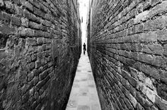 two people walking down an alley way in black and white, with one person standing on the other side