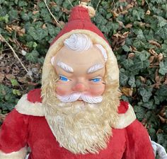 a santa clause doll sitting in front of some bushes