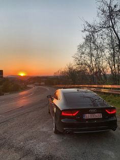 the car is parked on the side of the road as the sun sets in the background