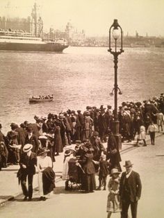 an old black and white photo of people walking on the beach with boats in the background