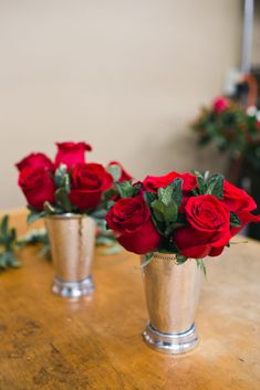 three silver vases filled with red roses on top of a wooden table in a room