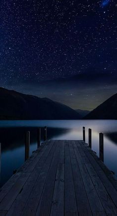 the night sky is lit up with stars above a dock on a body of water