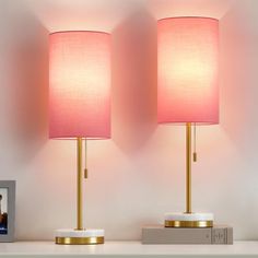 two pink lamps sitting on top of a white shelf