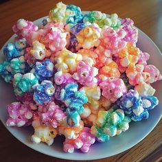 there is a white plate filled with colorful popcorns on top of a wooden table