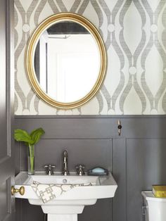 a white sink sitting under a round mirror in a bathroom next to a wall mounted toilet