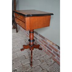 an old wooden table with a drawer on it's top and a brick wall in the background