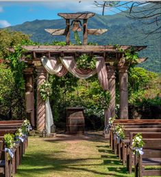 an outdoor wedding setup with wooden chairs and flowers on the aisle, surrounded by greenery