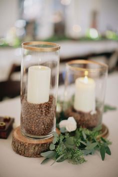 two glass vases with candles and flowers on a table