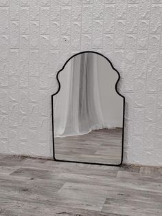 a mirror sitting on top of a wooden floor next to a white wall with a black frame