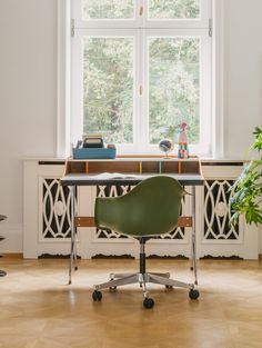 a green chair sitting in front of a window next to a desk with a laptop on it