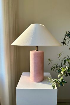 a pink lamp sitting on top of a white table next to a potted plant