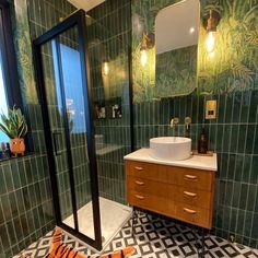 a bathroom with green and black tiles on the floor, sink, mirror and shower stall