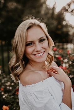 a woman with blonde hair and blue eyes smiles at the camera while standing in front of flowers