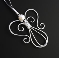 a white necklace with an intricate design and pearl bead hanging from it's center