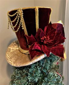 "This tree topper top hat is sold, but no worries we can make one just for you This elegant burgundy and gold tree topper top hat and or centerpiece is a must have. The top hat tree topper is made as follows: *The top hat taper/body is made with burgundy velvet fabric and adorned with gold braids throughout the hat. Decorated with: *Burgundy poinsettia with glittered edging. The front of the top hat is adorned with looped gold beads. The bow is adorned with a gold sequence Christmas ornament. *T Gold And Burgundy Christmas Tree, Christmas Hats Ideas Diy, Burgundy Christmas Tree, Top Hat Centerpieces, Top Hat Tree Topper, Gold Braids, Snowman Tree Topper, Gold Tree Topper, Burgundy Christmas