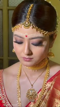 a woman in a red and gold sari with jewelry on her head, looking down at the camera