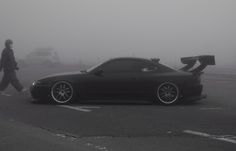 a black sports car parked on the side of a foggy road with a man walking past it